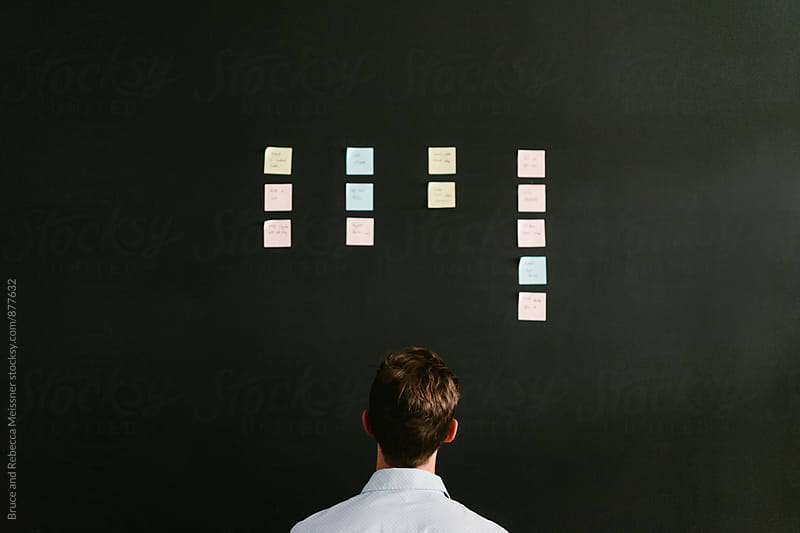 The focus of OKRs is connecting company, team and personal objectives to measurable results. Photo of a man staring at PostIt notes on the wall
